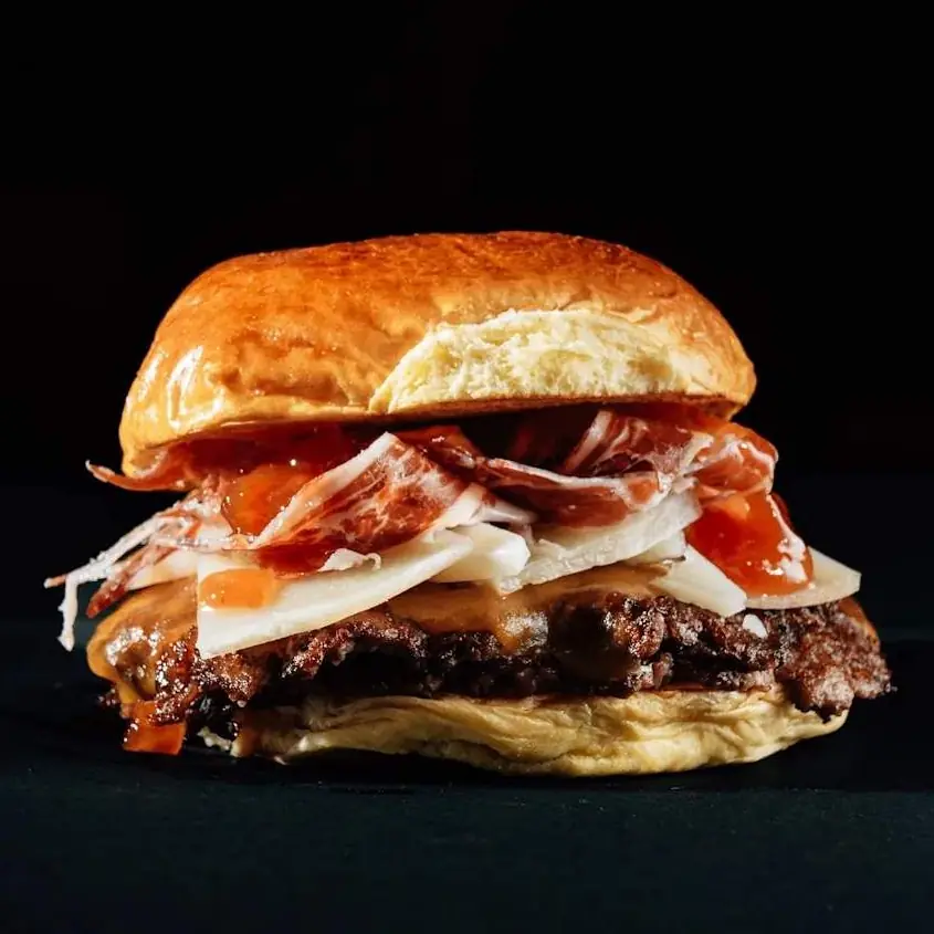 Hamburguesa Ibérica: doble carne smash con cheddar ahumado, jamón serrano, queso curado, confitura de tomate y mayo Big Boss